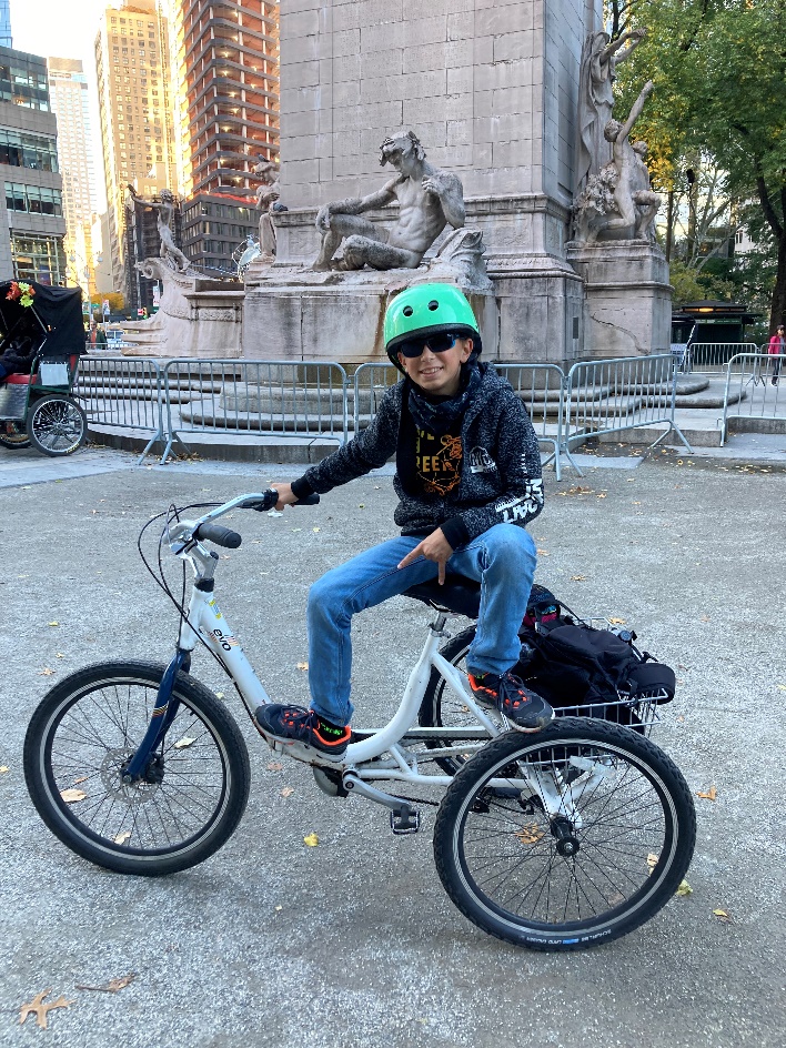 un garçon pose sur un vélo devant une statue à Central Park